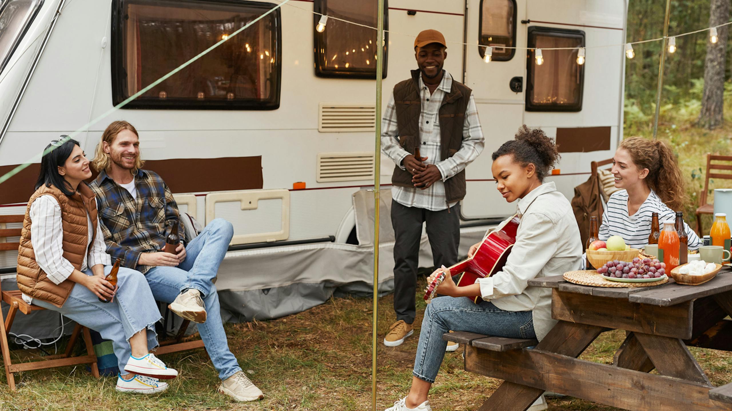 Jeunes jouant de la guitare à l’extérieur d'une caravane dans un camping
