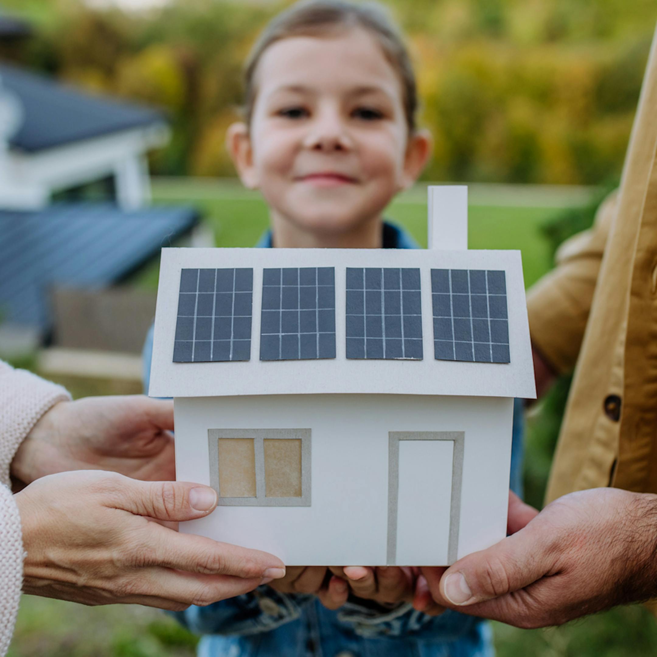 Gros plan d’une jeune famille tenant un modèle de maison en papier avec des panneaux solaires.