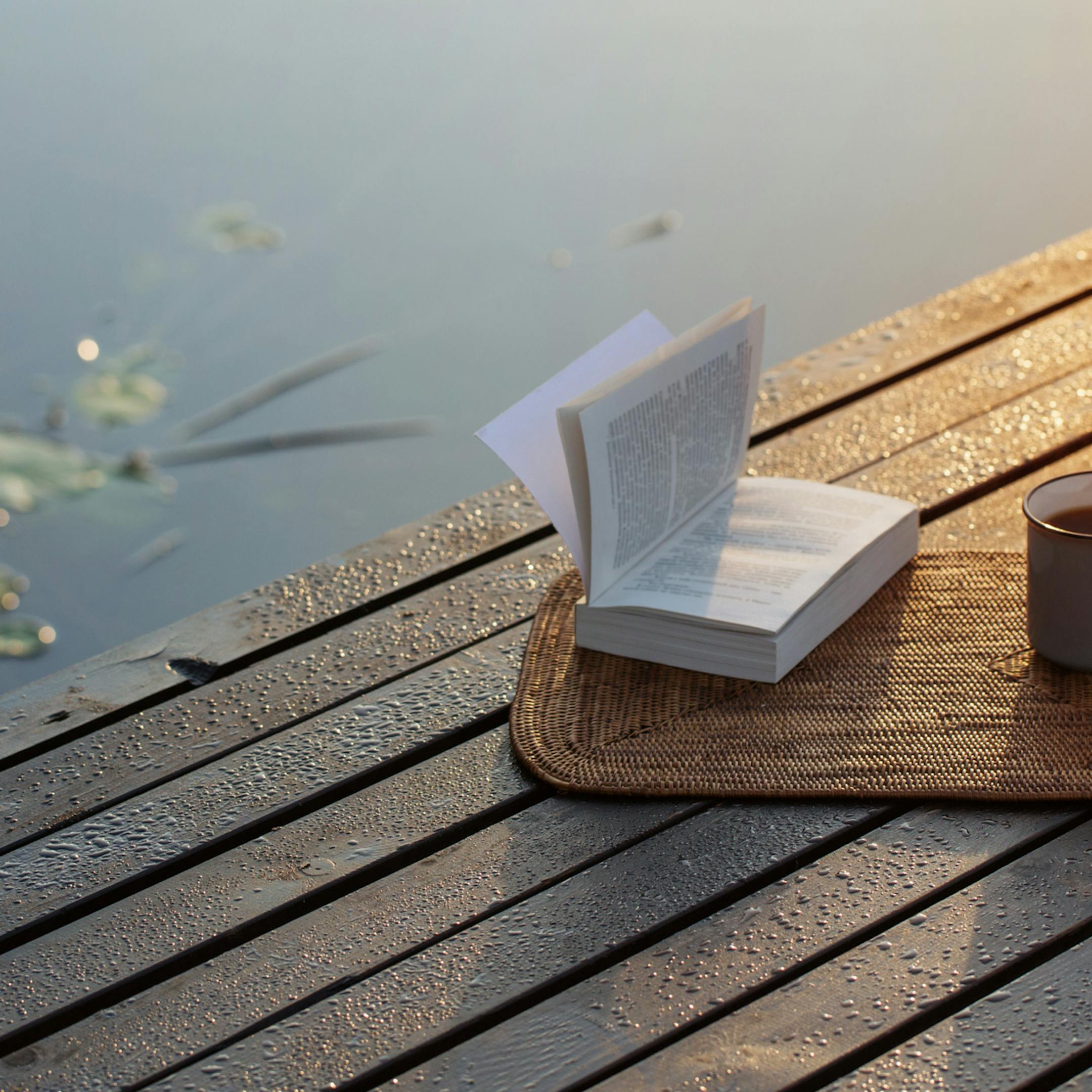 Plateau posé sur un ponton avec un livre et un thé au soleil couchant