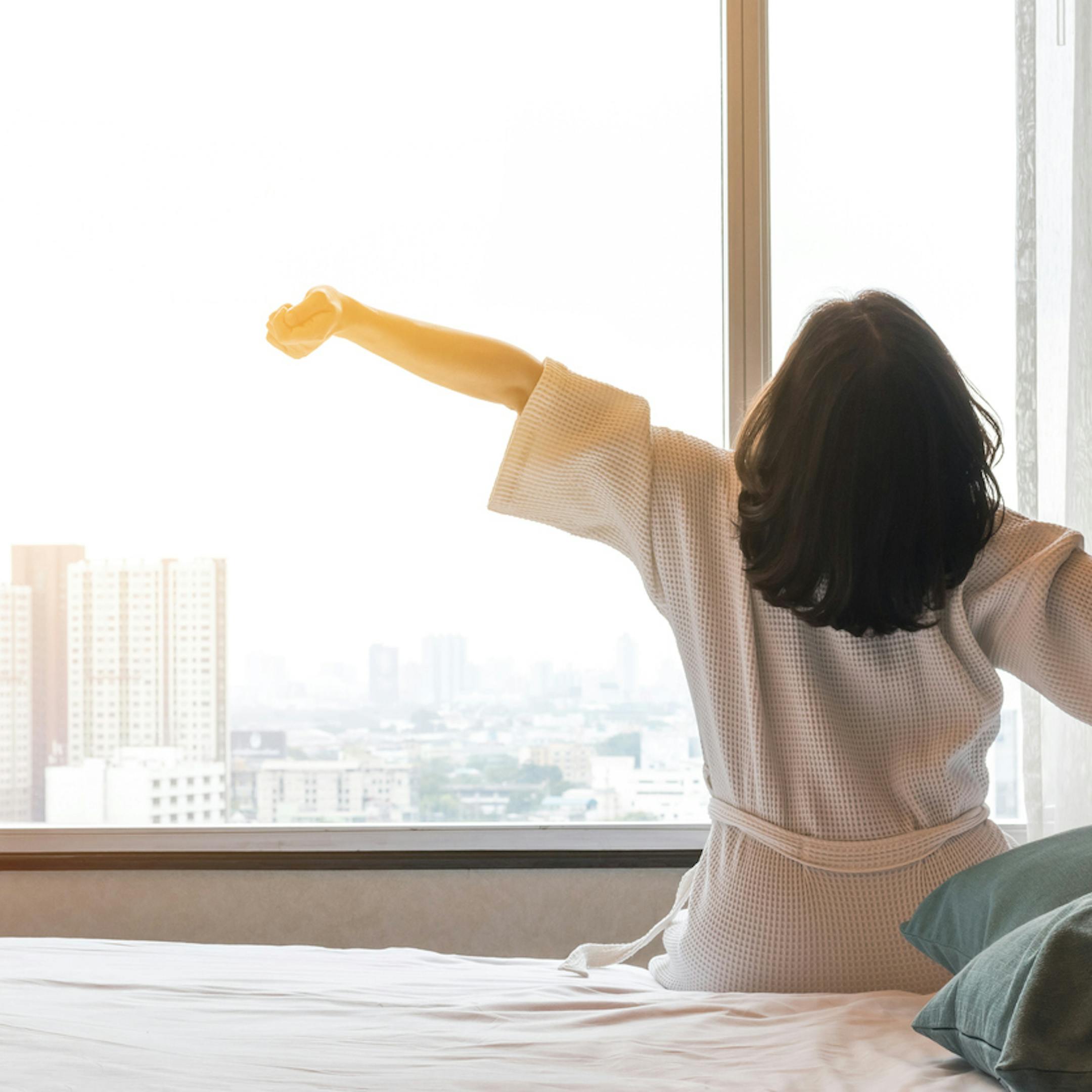 Femme s'étirant au saut du lit dans une chambre d'hôtel de luxe en ville
