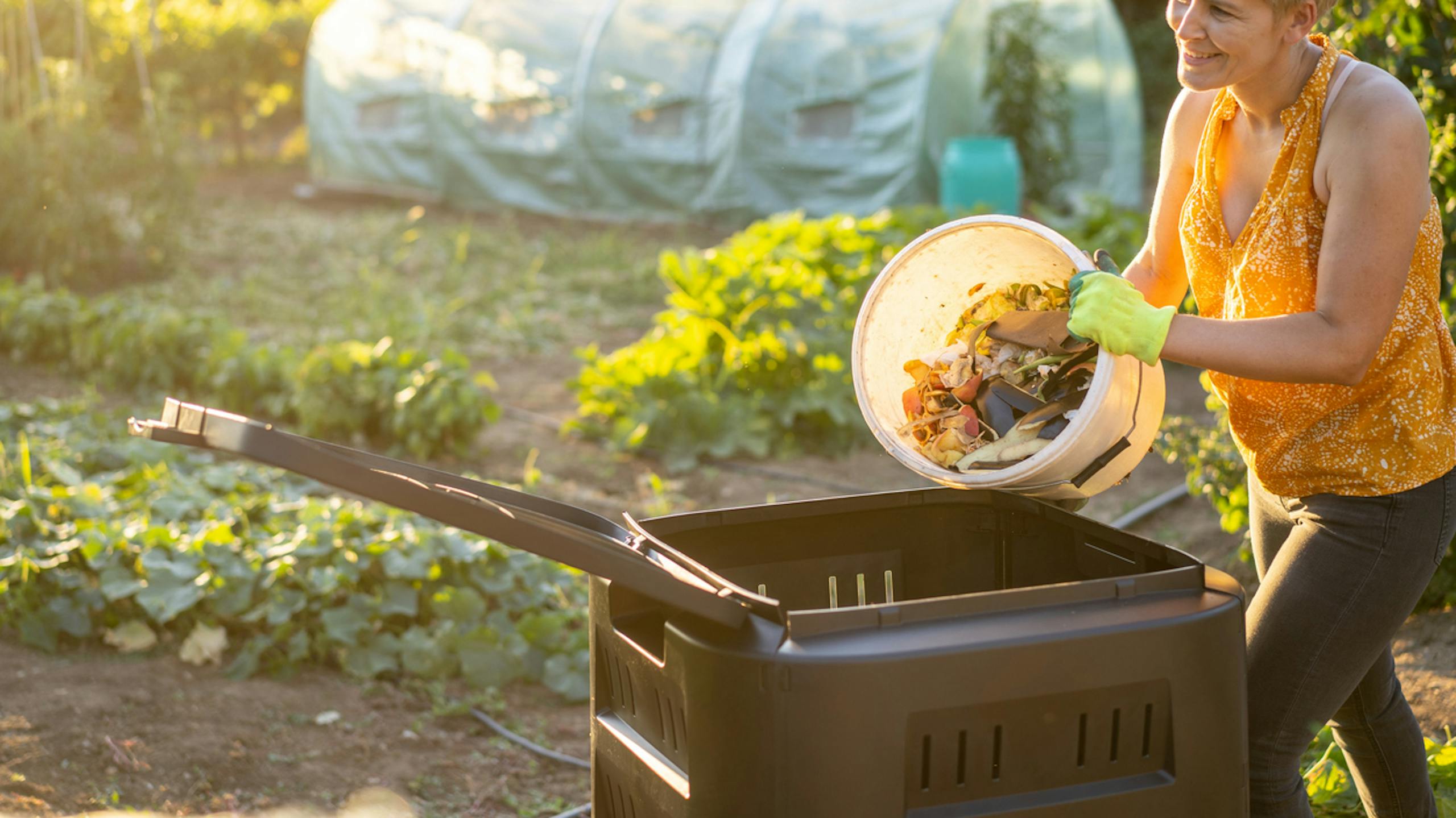 Femme qui jette ses déchets alimentaires dans un composteur de jardin à la maison