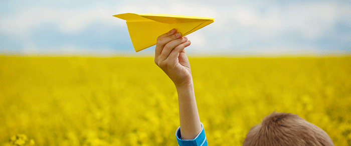 Photo d'un enfant devant un champ avec un avion en papier