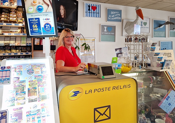 Postière dans un bureau de Poste derrière un desk "La Poste Relais"