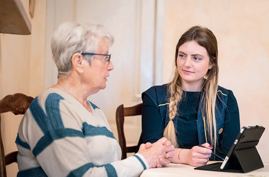 Photo d'une postière avec une dame âgée, assises autour d'une table, avec une tablette