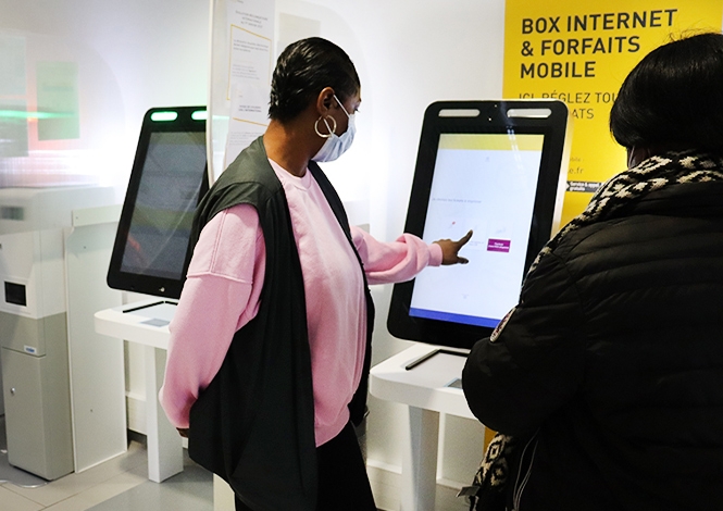 Photo d'une femme devant une borne numérique en bureau de Poste