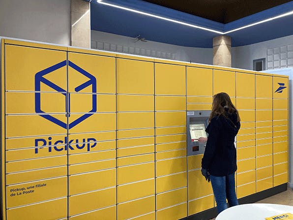 une femme retire un colis devant une consigne pickup