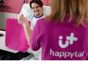Photo d'un patient souriant dans un lit d'hôpital en compagnie d'un concierge happytal