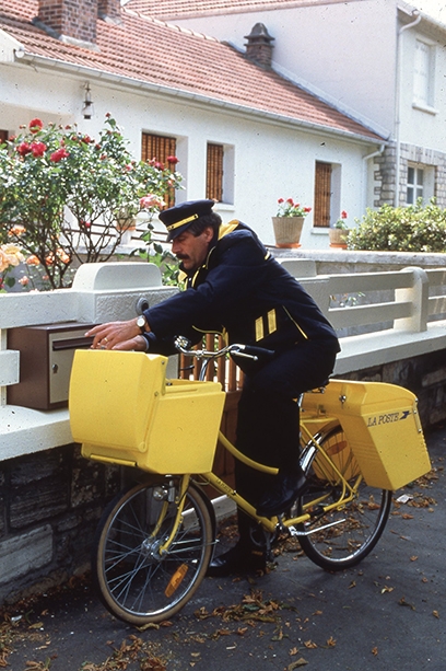 Photo d'un facteur à vélo qui dépose du courrier dans une boîte aux lettres