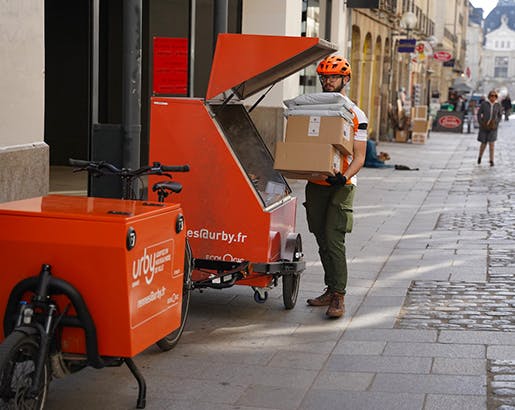 un facteur charge son vélo cargo de colis dans la rue