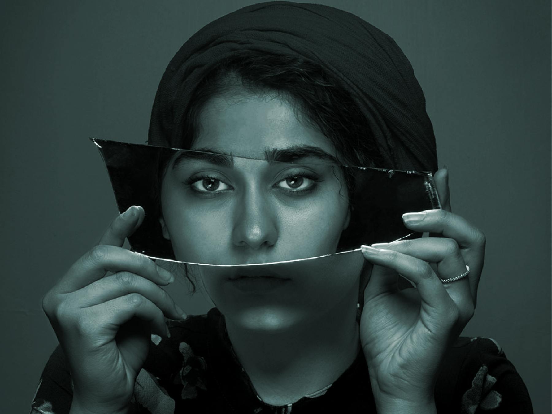 Woman holding broken mirror over eyes