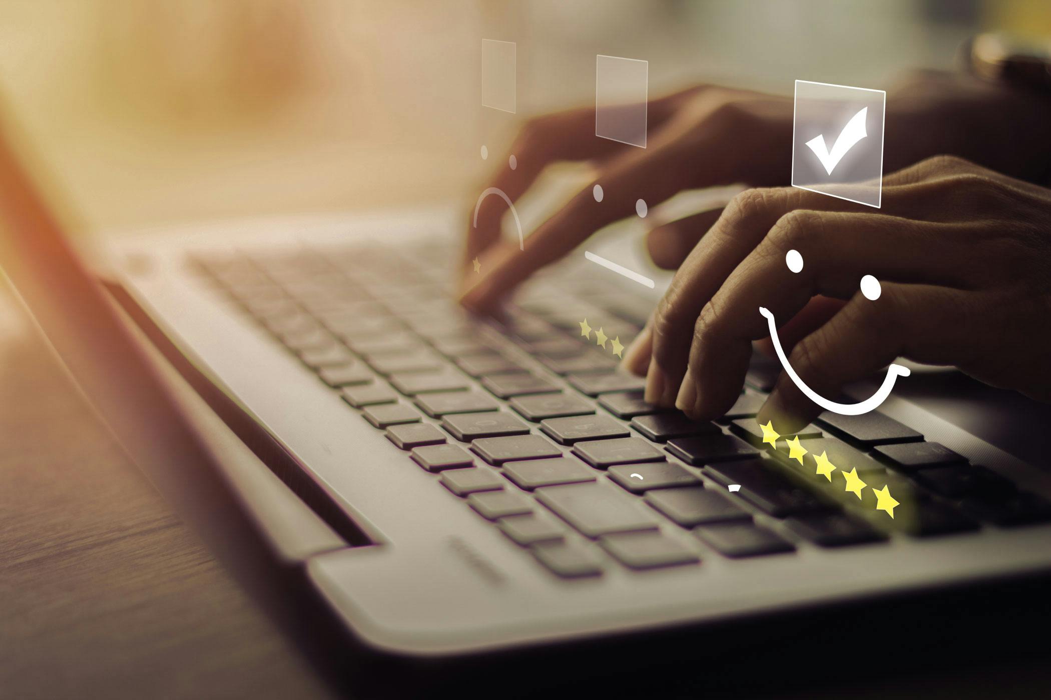 Close-up of person typing on a laptop and selecting a smiley face icon with five stars.