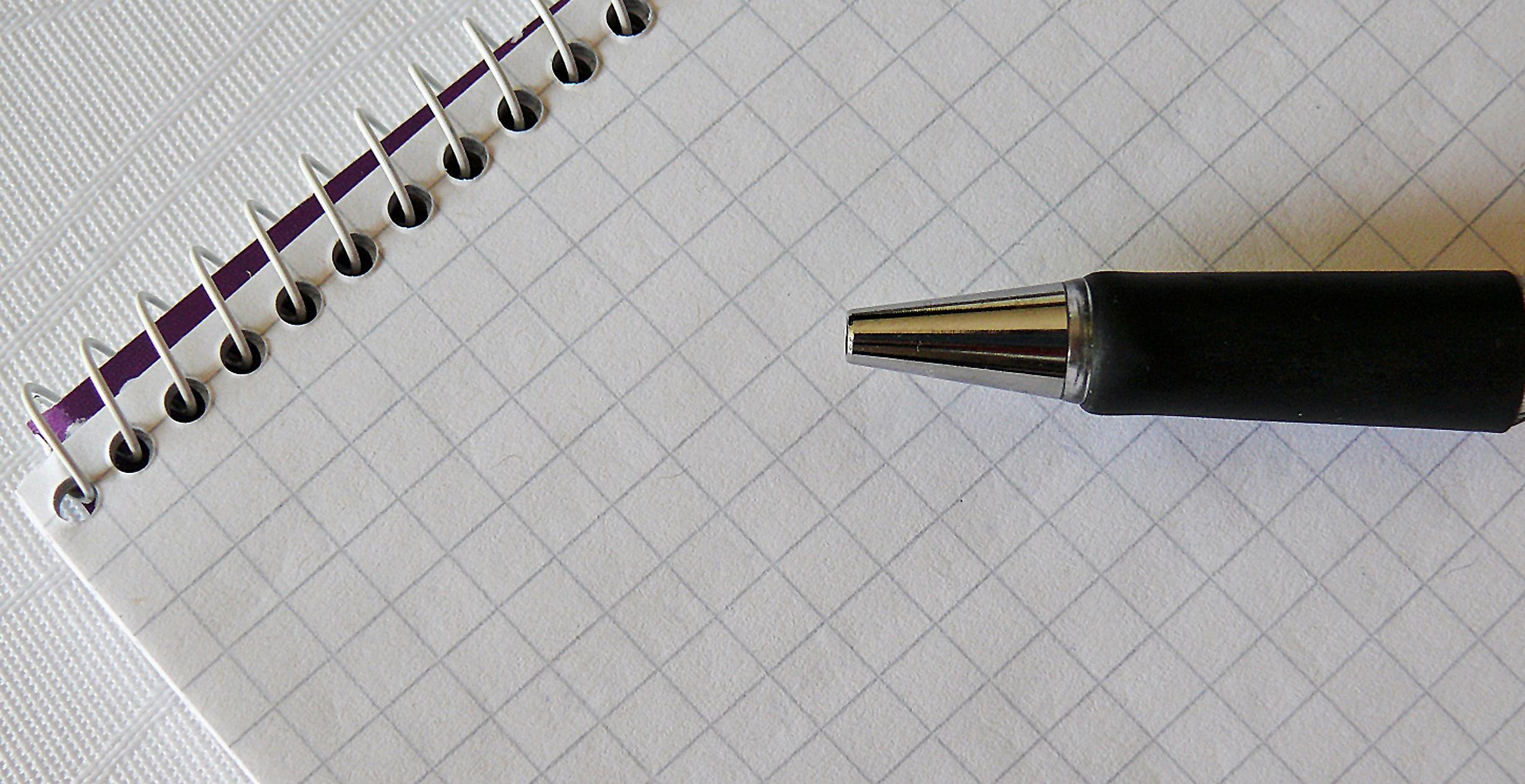 Close-up of a spiral bound notebook of graph paper and a pen