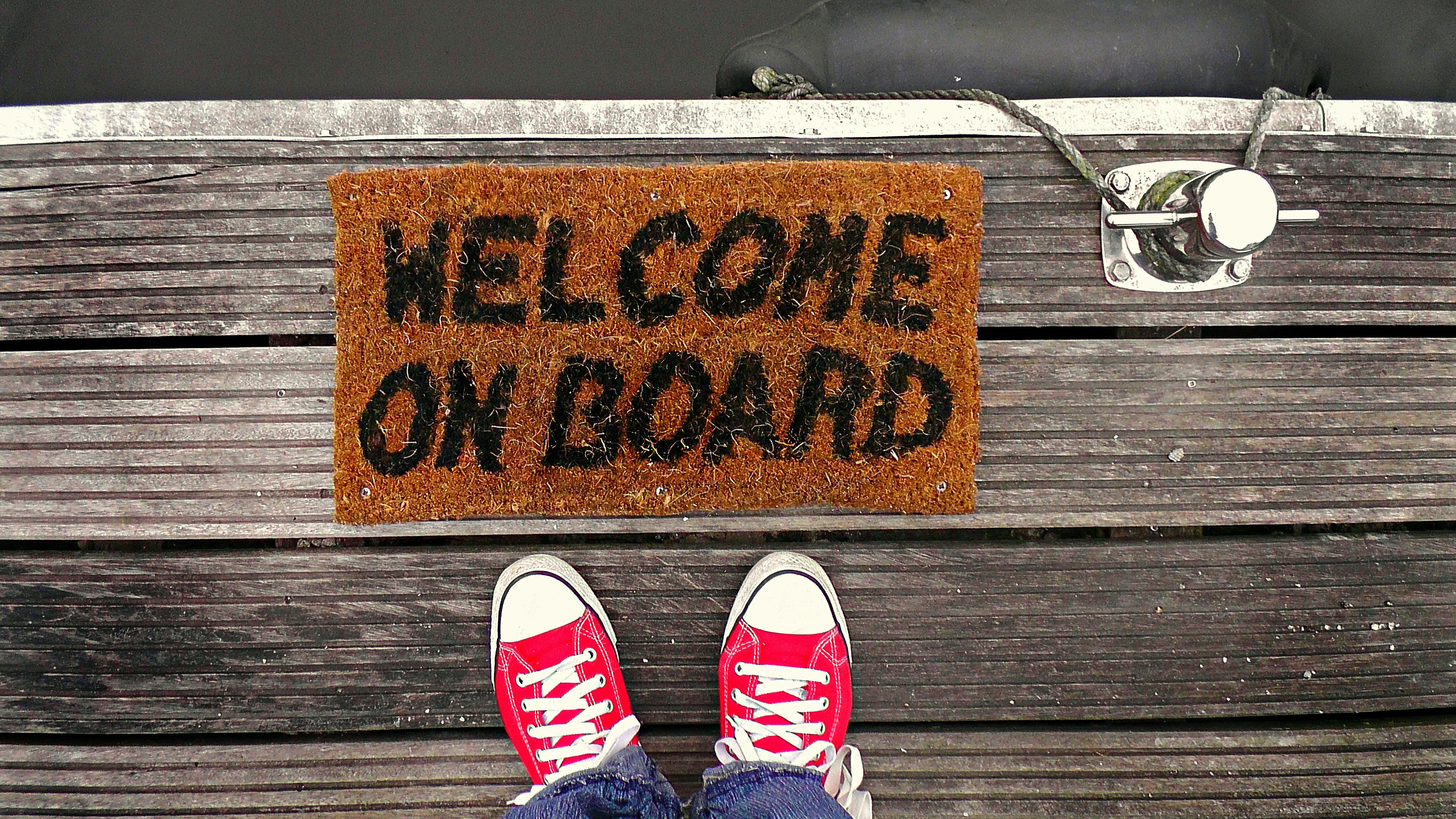 Close-up of two-shoes standing in front of a "Welcome on board" welcome mat