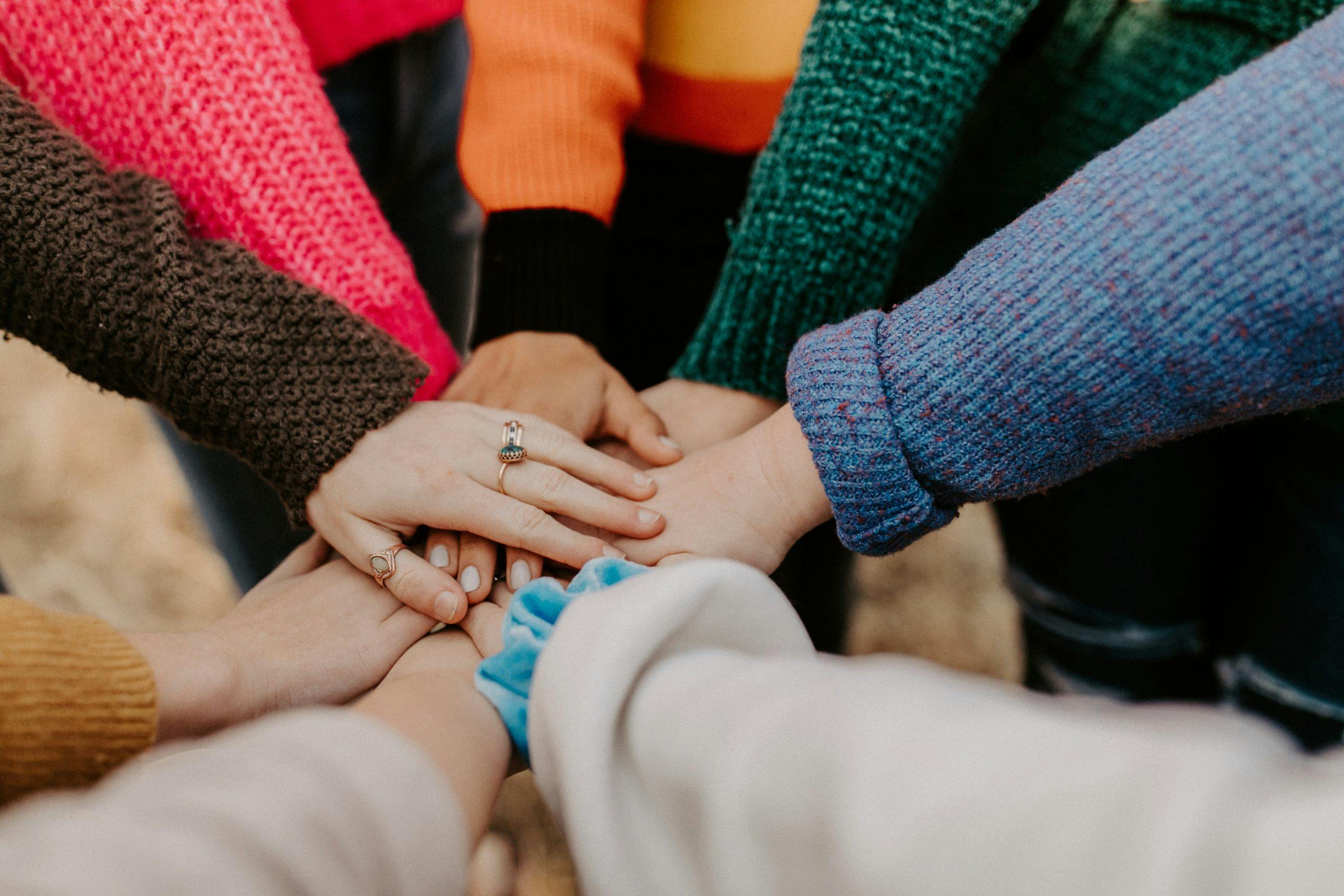 People in colorful sweaters gather hands for a huddle.