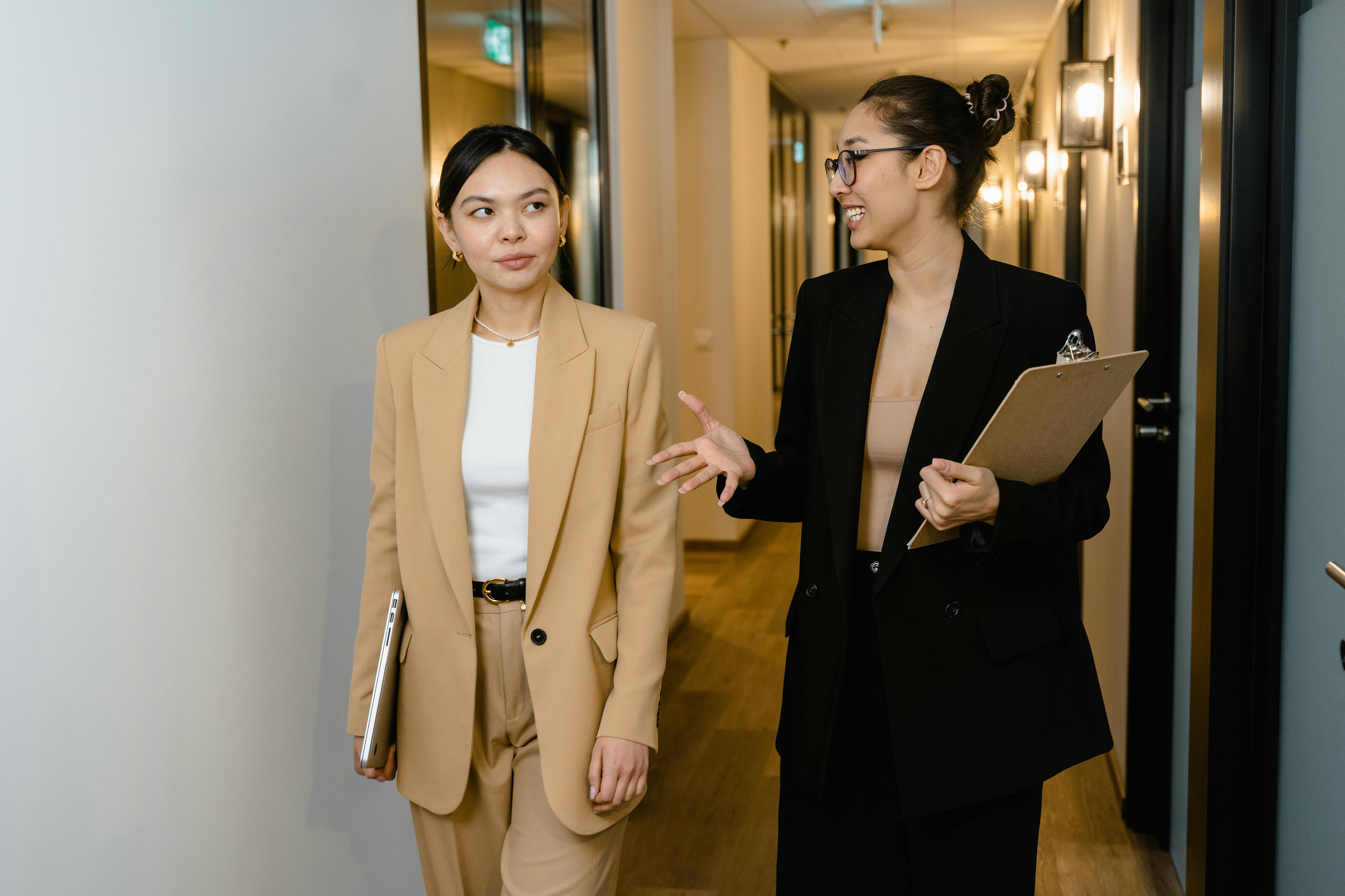 Two women walking in a hallway with clipboard having a conversation