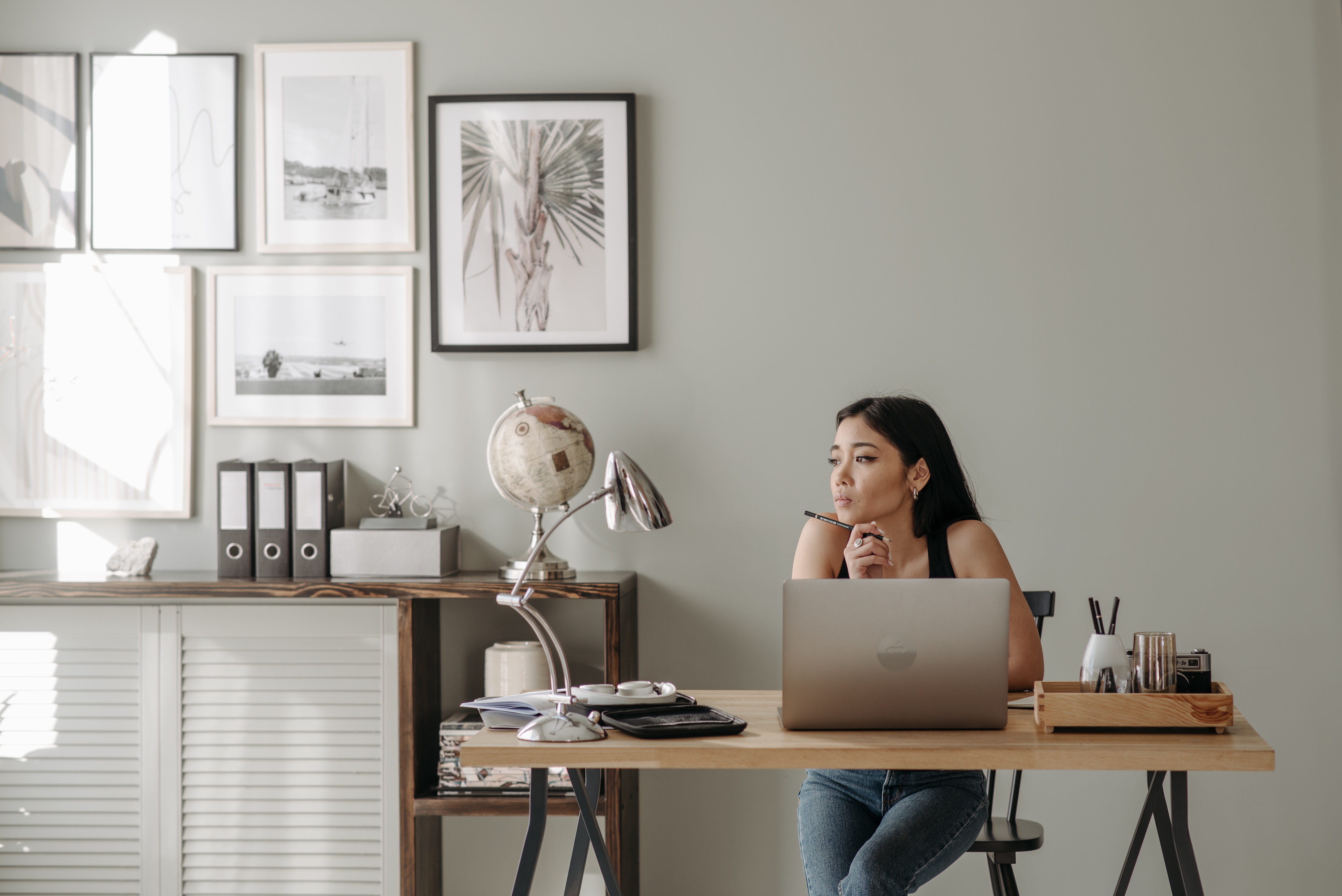Woman sitting at desk, with picture frames on the wall behind her, looking away from computer.