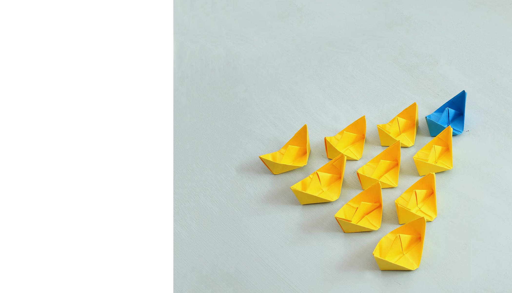 Photo of blue paper boat leading group of yellow paper boats