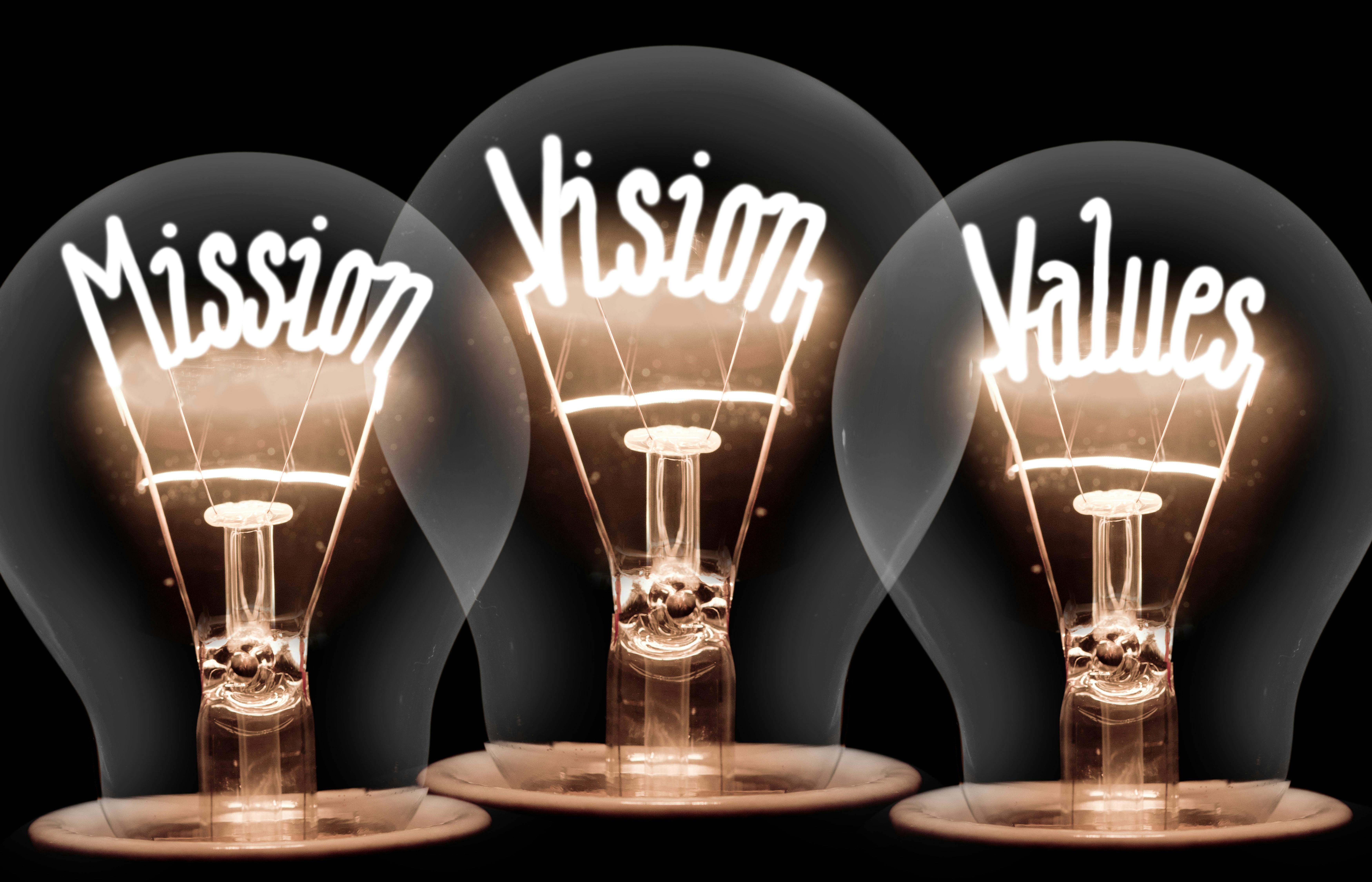 Three illuminated light bulbs display the words "Mission," "Vision," and "Values" in glowing text.