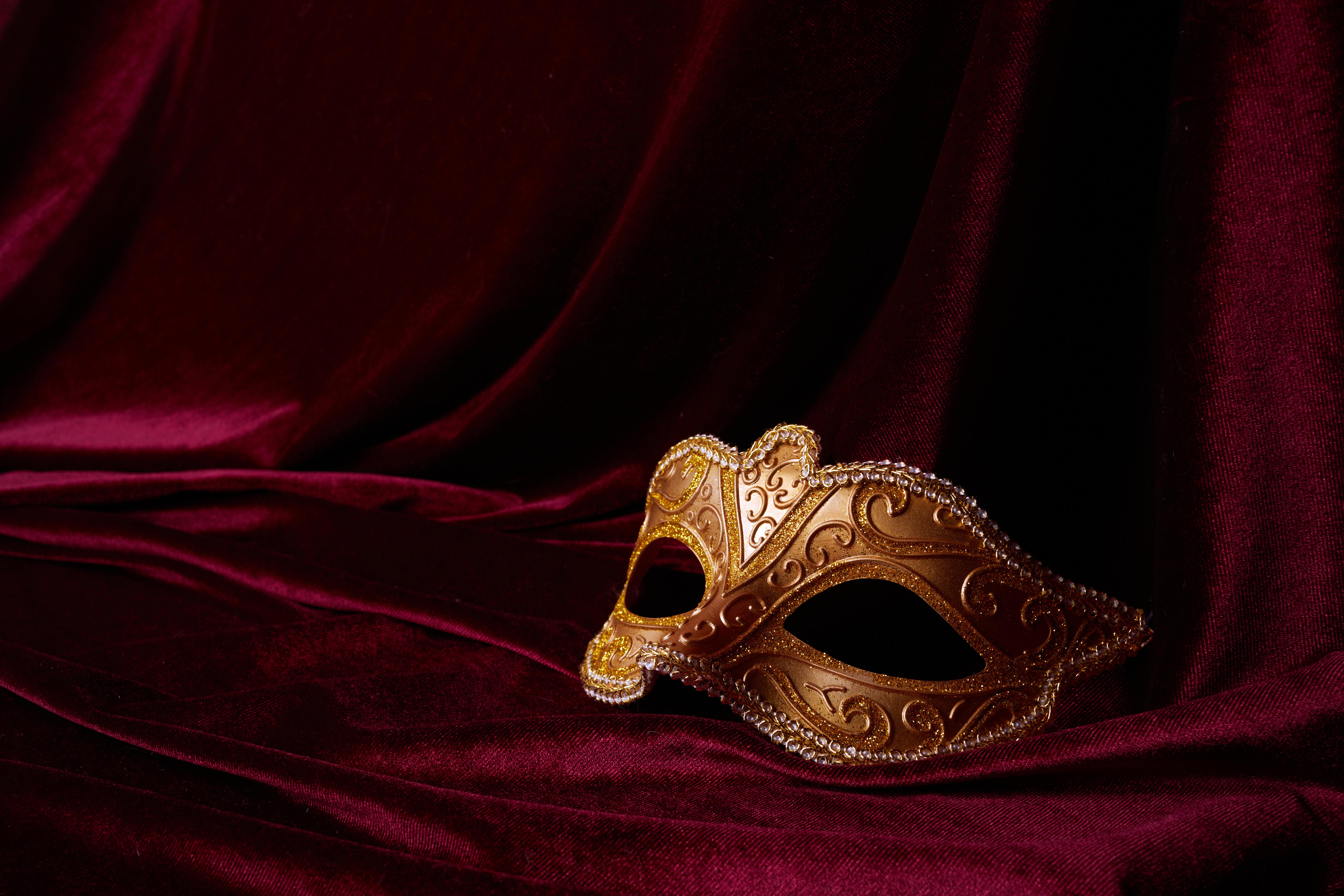 A mask is seen against a red velvet background.