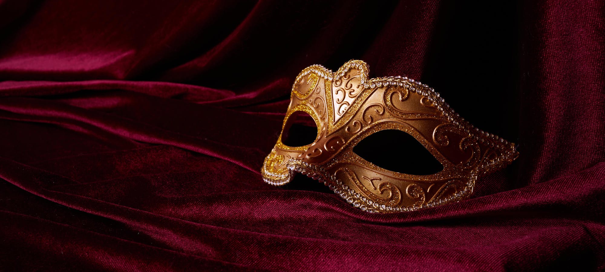 A mask is seen against a red velvet background.