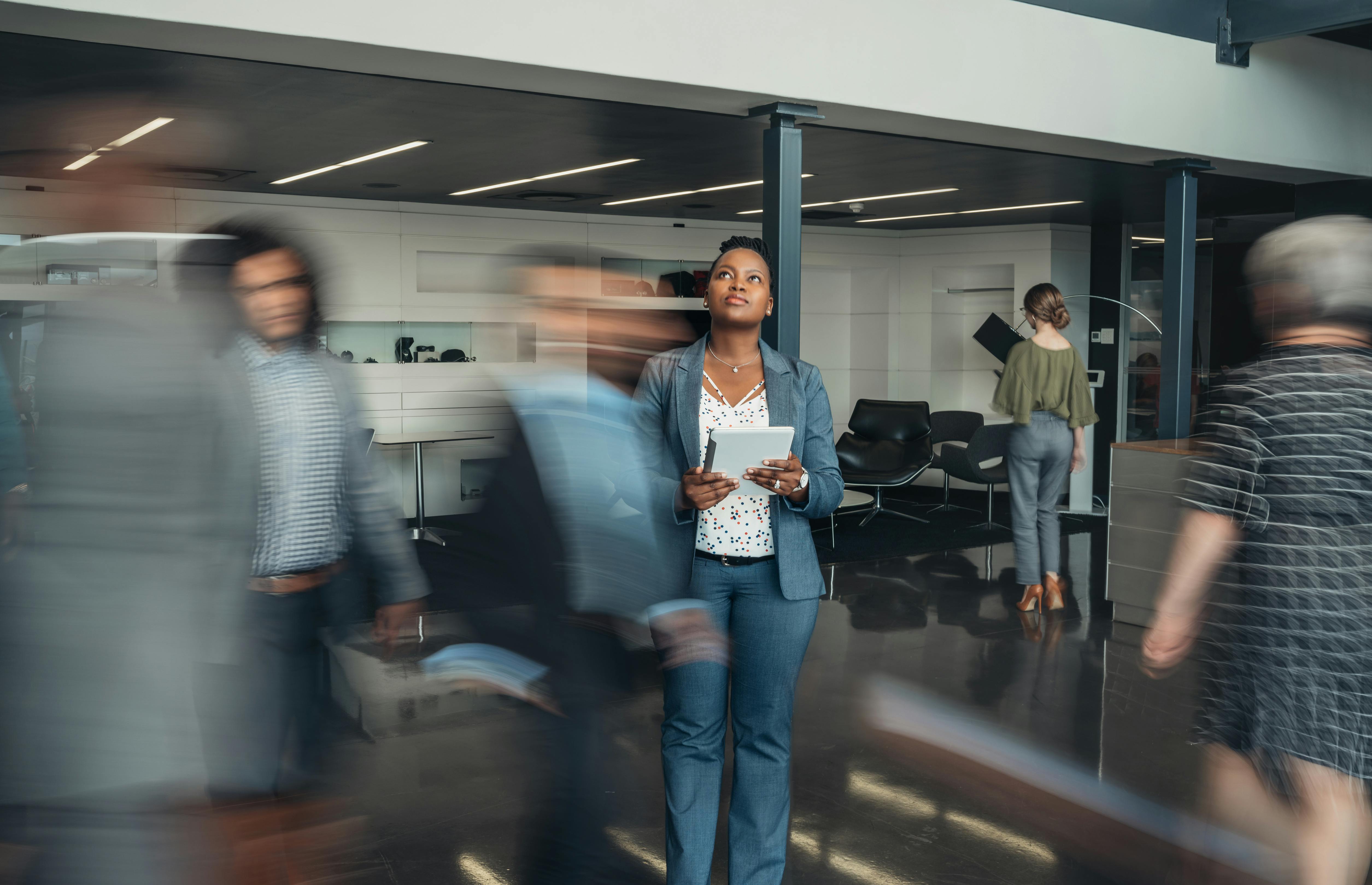 A woman stands and ponders in a busy office.