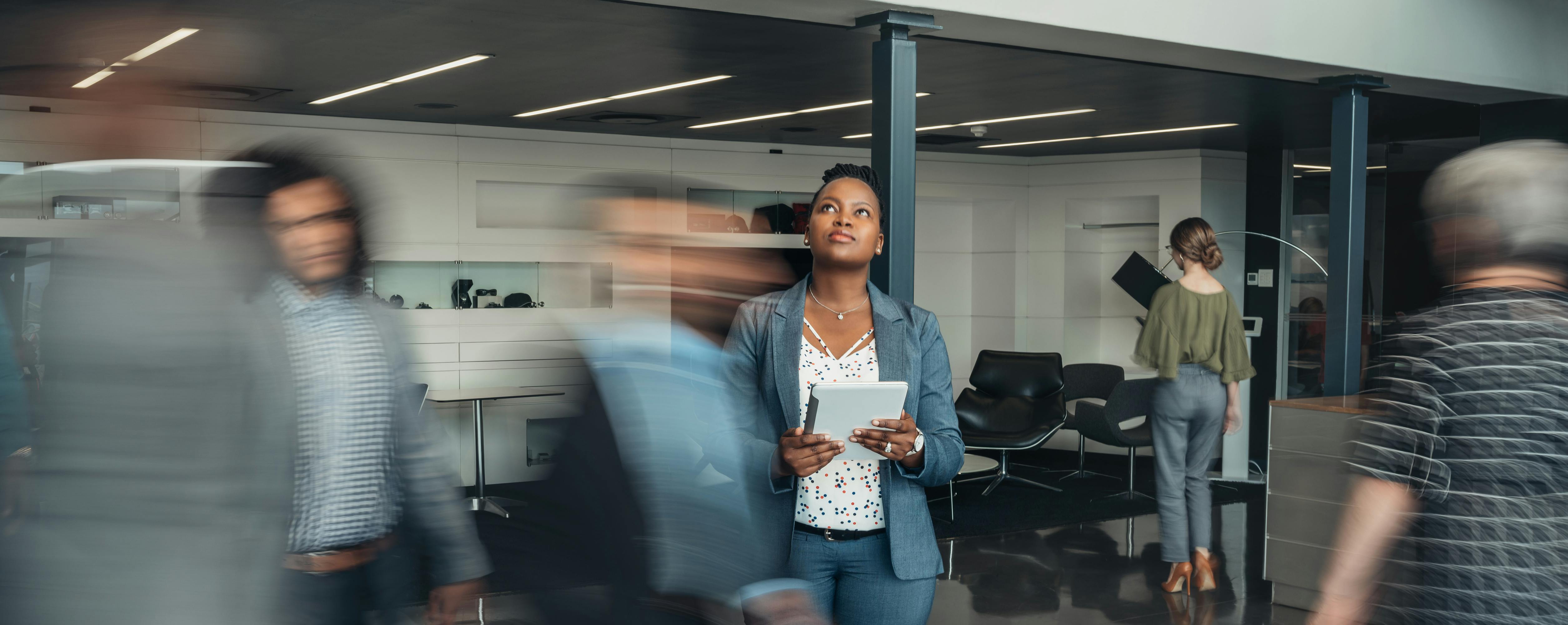A woman stands and ponders in a busy office.