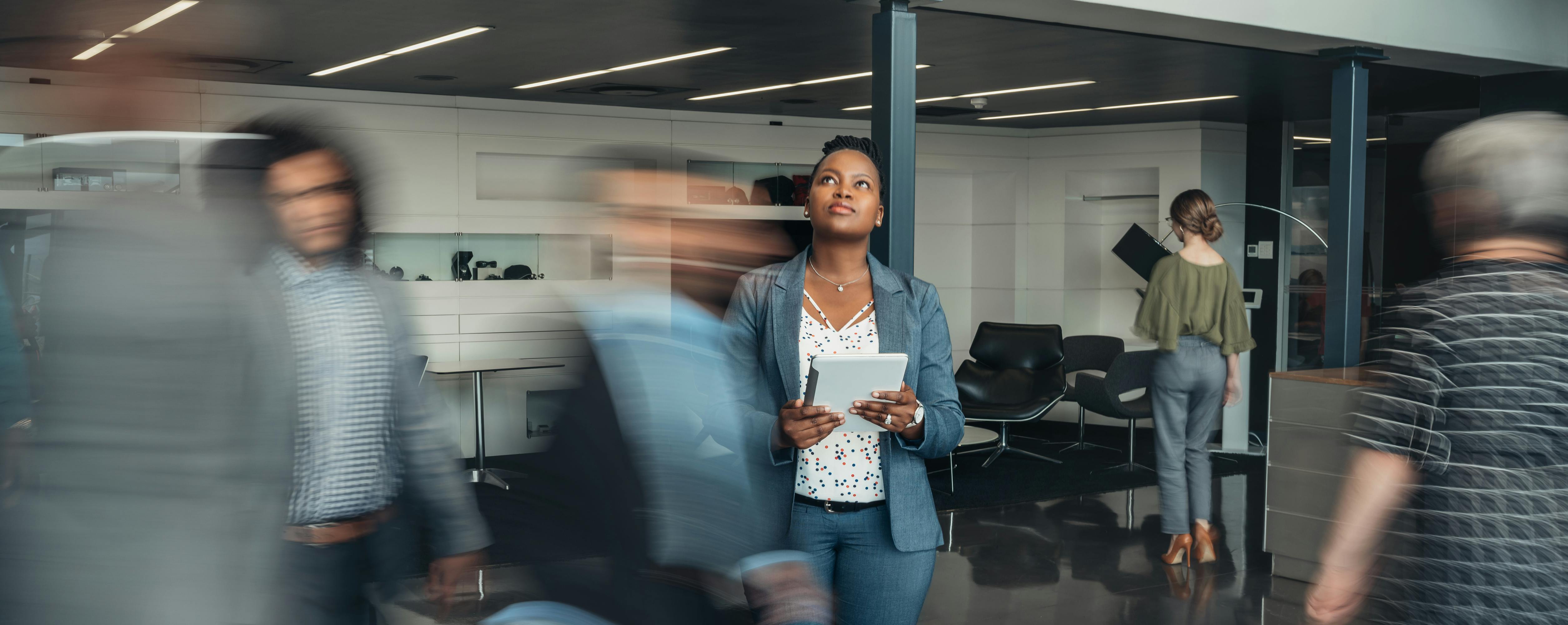 A woman stands and ponders in a busy office.