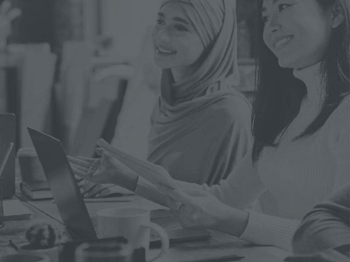 Two women smile in a workplace.