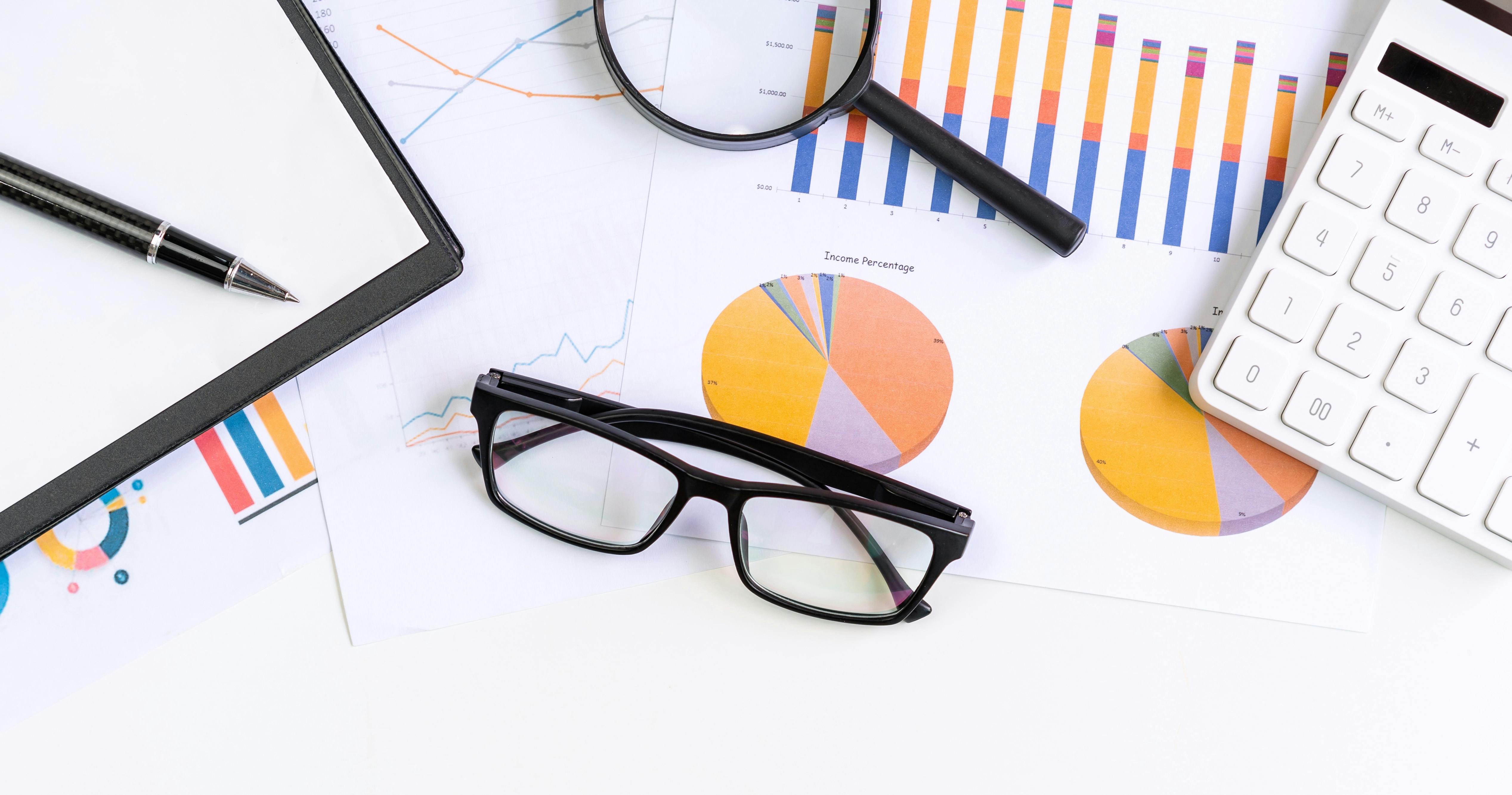 Glasses and office supplies lay atop graphs.