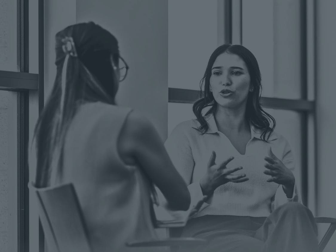 Two women are engaged in conversation in an office.