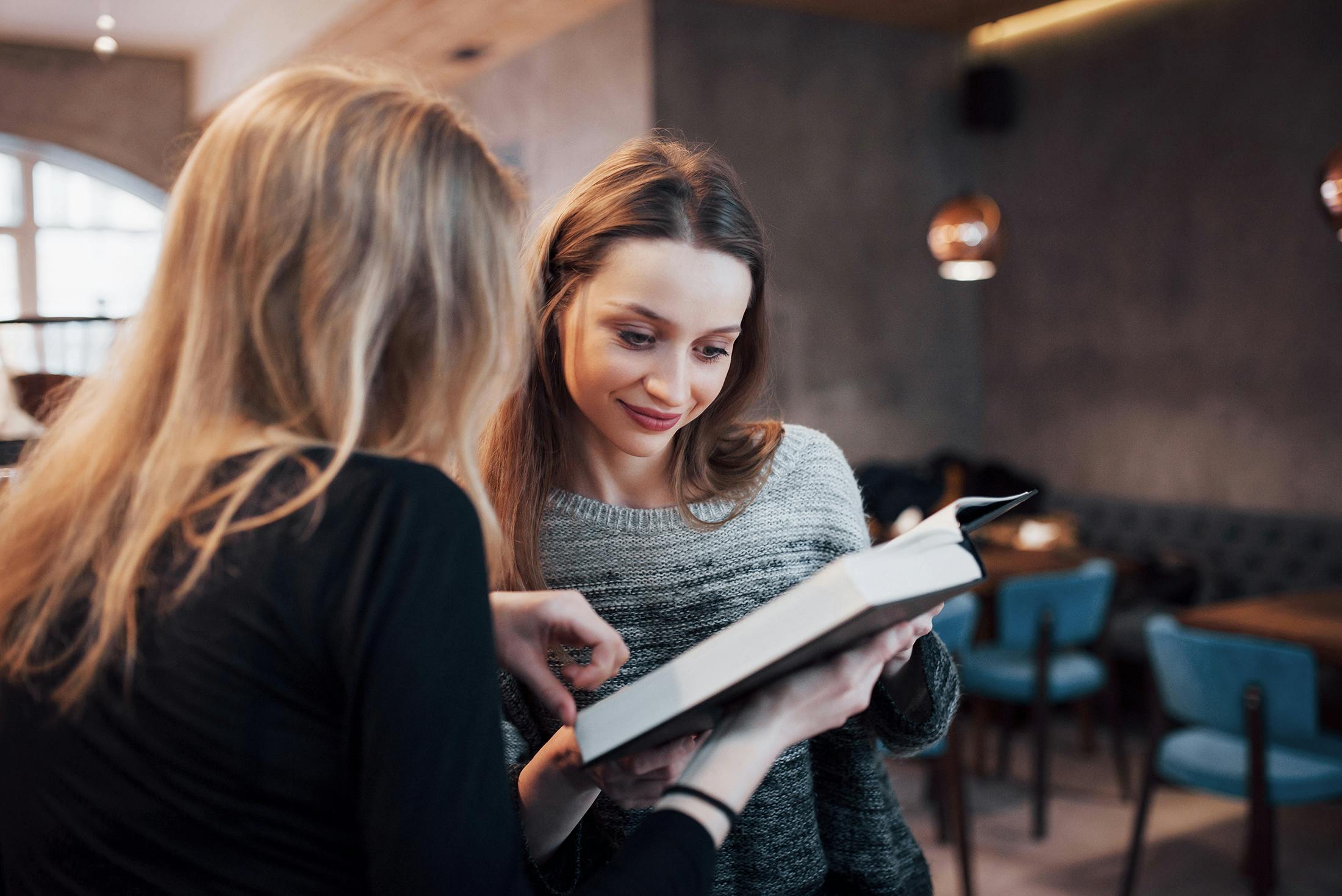 Two women engage in a discussion over a book in a cafe.