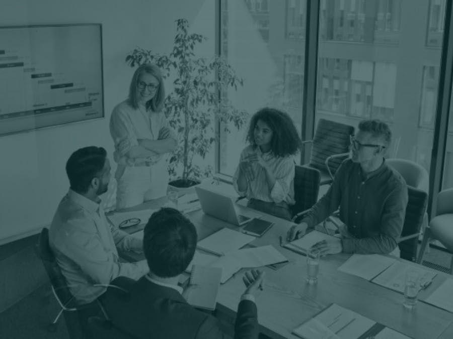 Five professionals are gathered around a conference table during a business meeting.