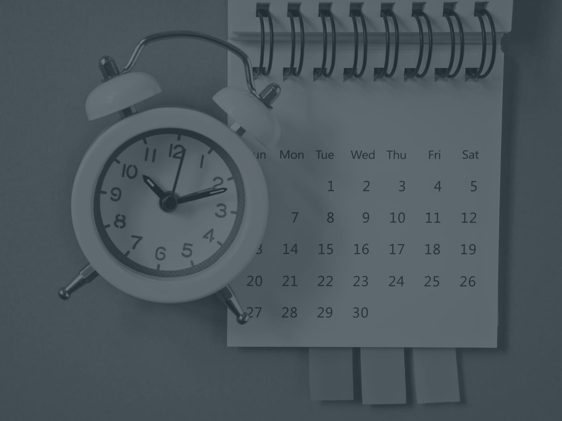 An alarm clock rests against a spiral calendar.