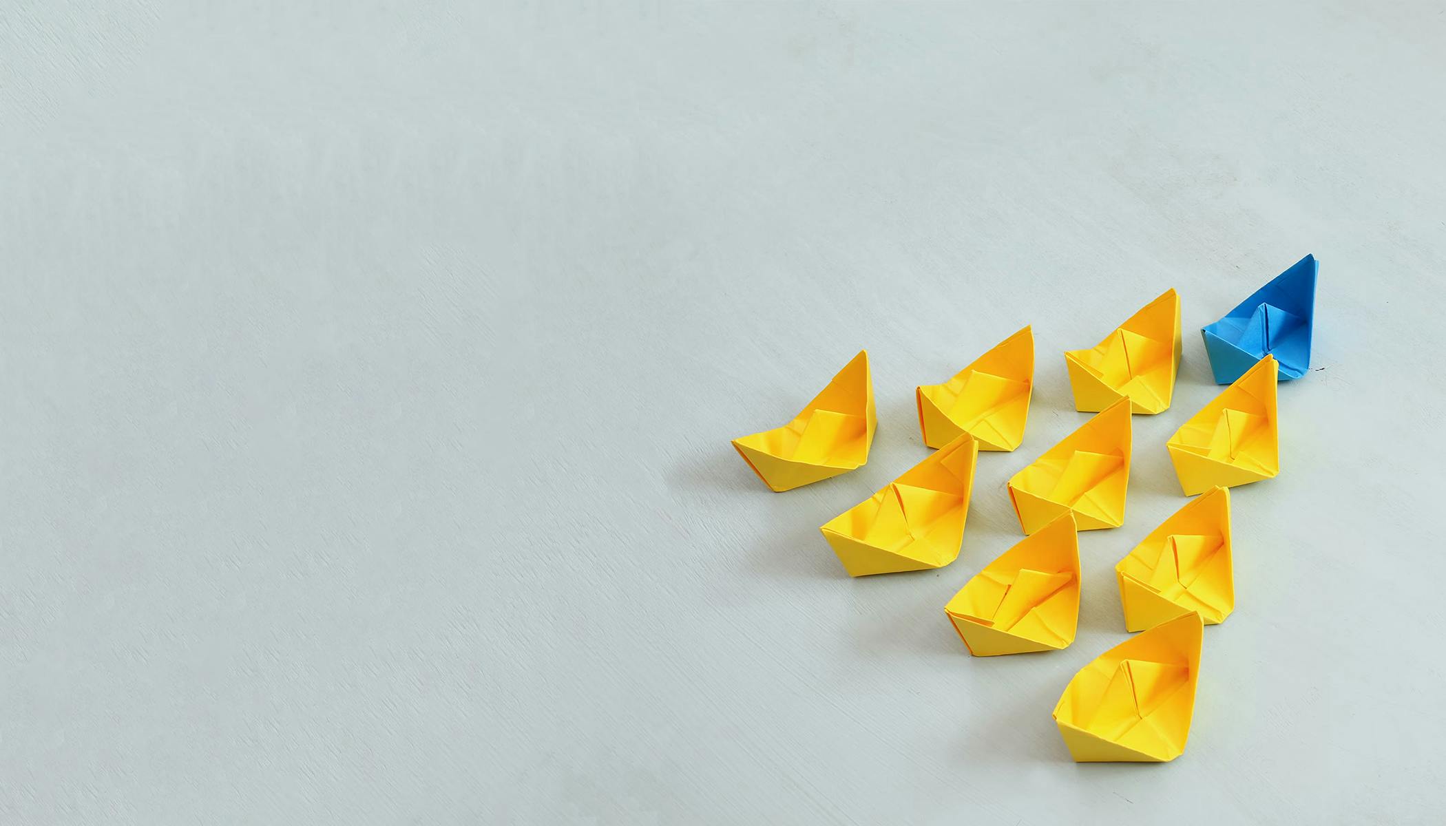 Photo of blue paper boat leading group of yellow paper boats