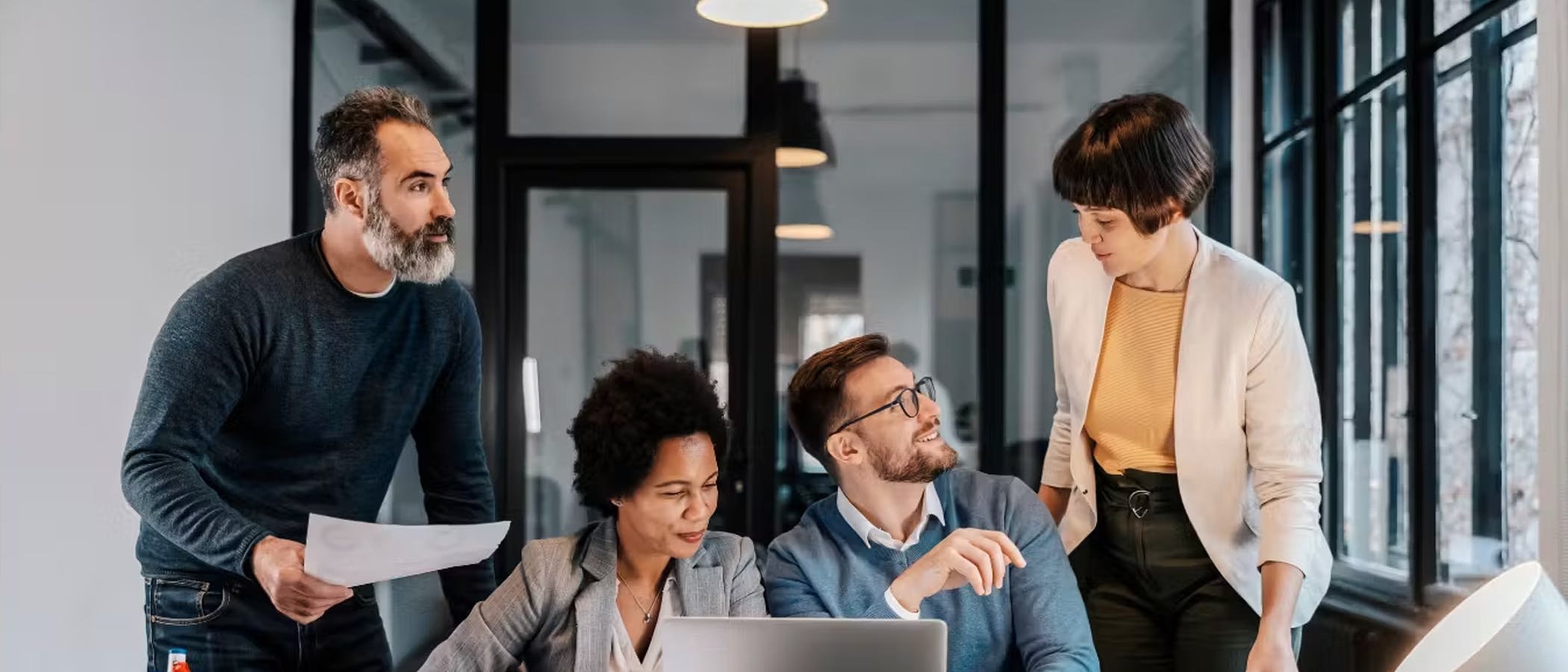 Employees talk animatedly in front of an open laptop.