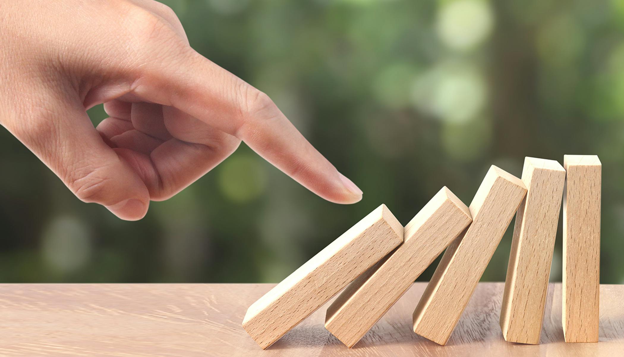 A hand topples over wooden dominoes.