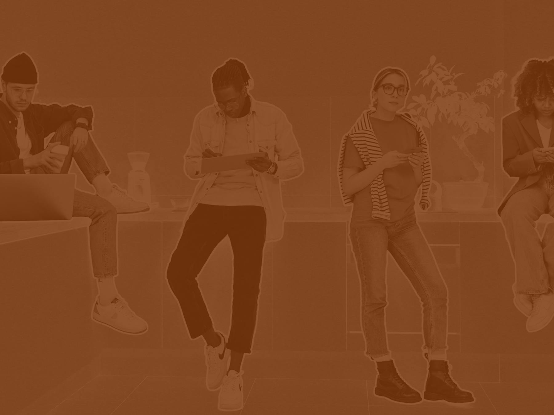 Four people in casual clothing using laptops, tablets, and phones while sitting and standing in a modern space.