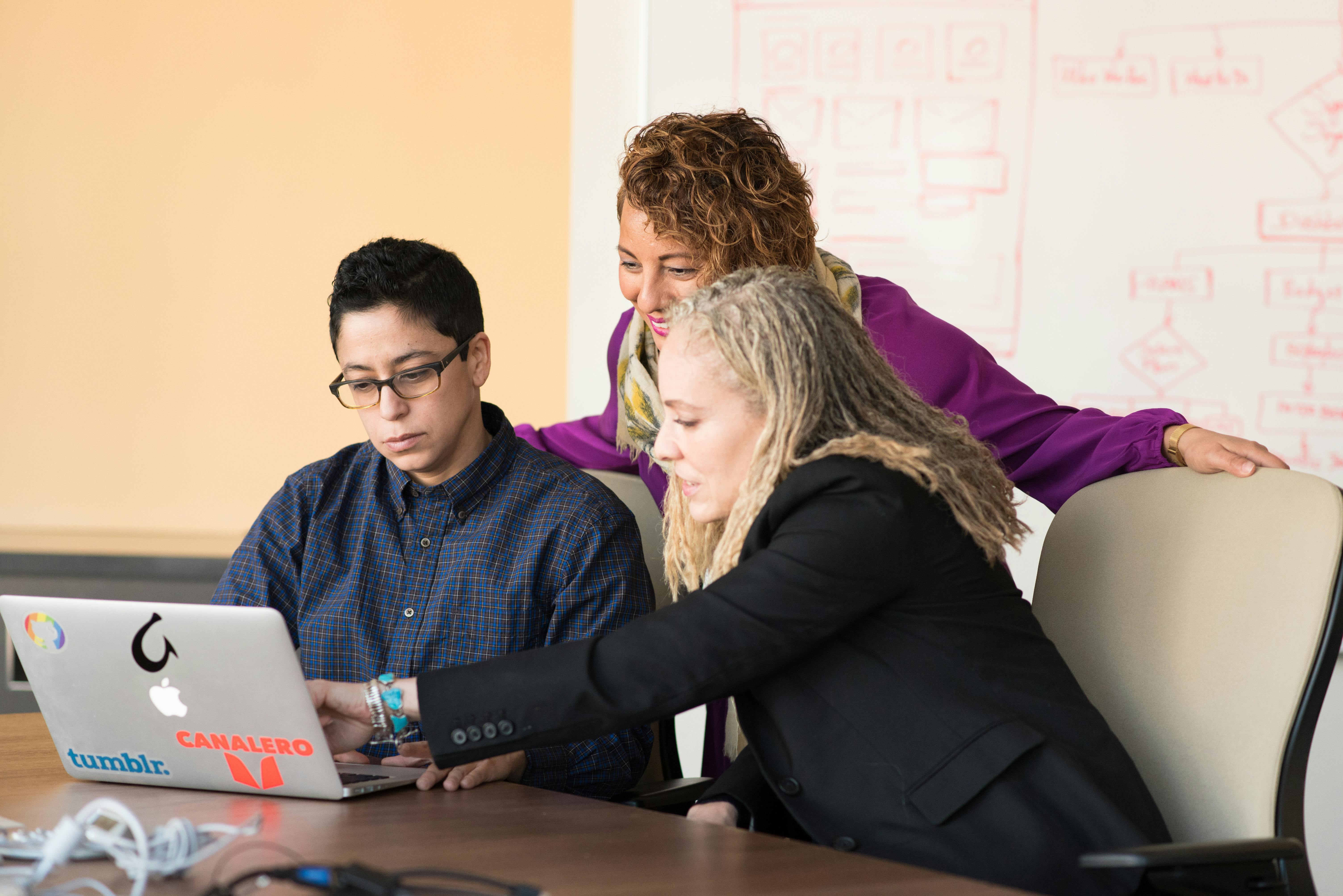 Three people look at a laptop.