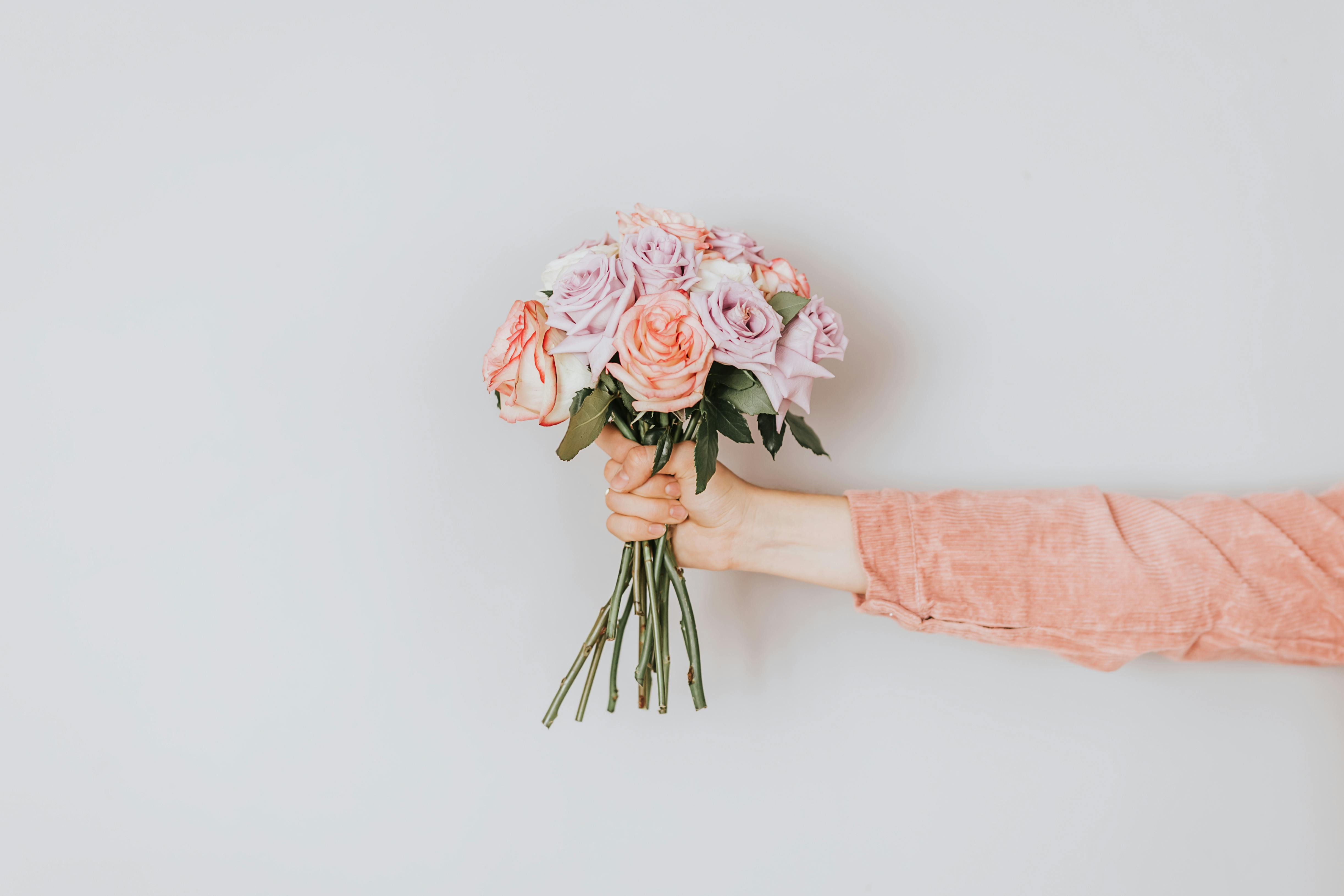 A hand extends from the right, holding a small bouquet of roses against a plain white background.