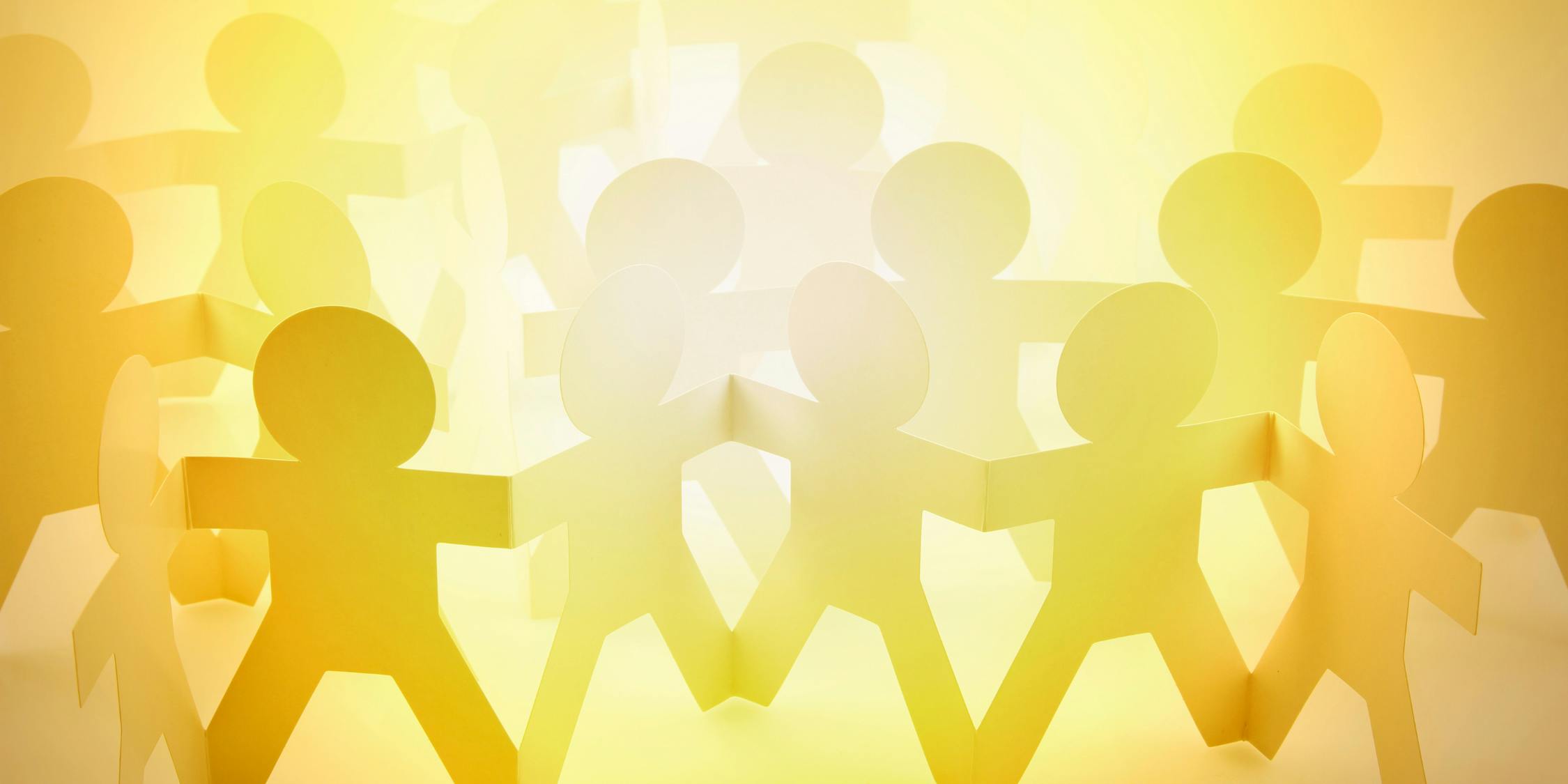 A chain of backlit paper-cutout people holding hands.