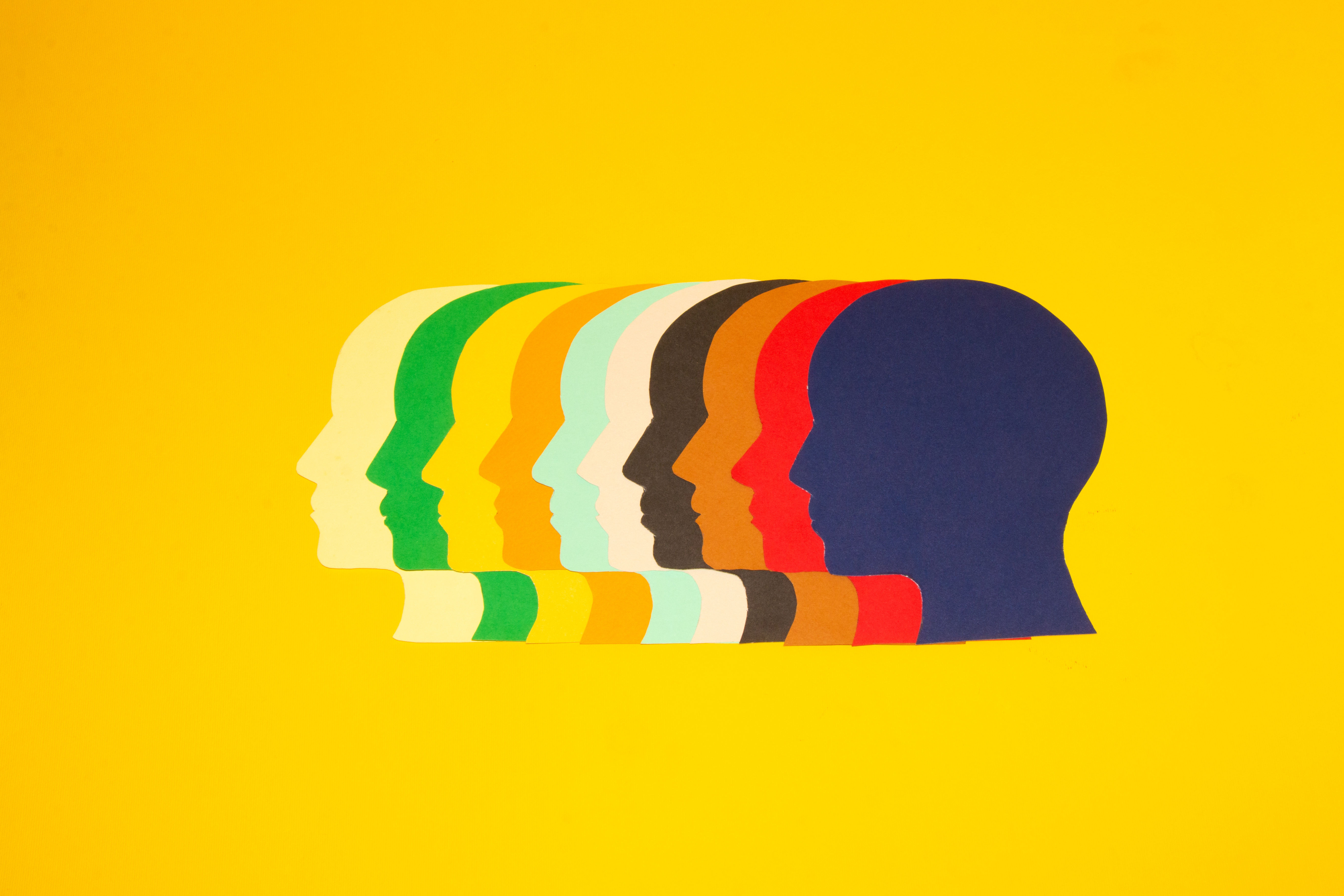 Colorful paper heads looking at one point on a yellow background.