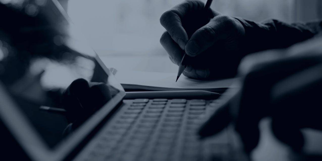 A person types on a laptop while writing with a pencil.