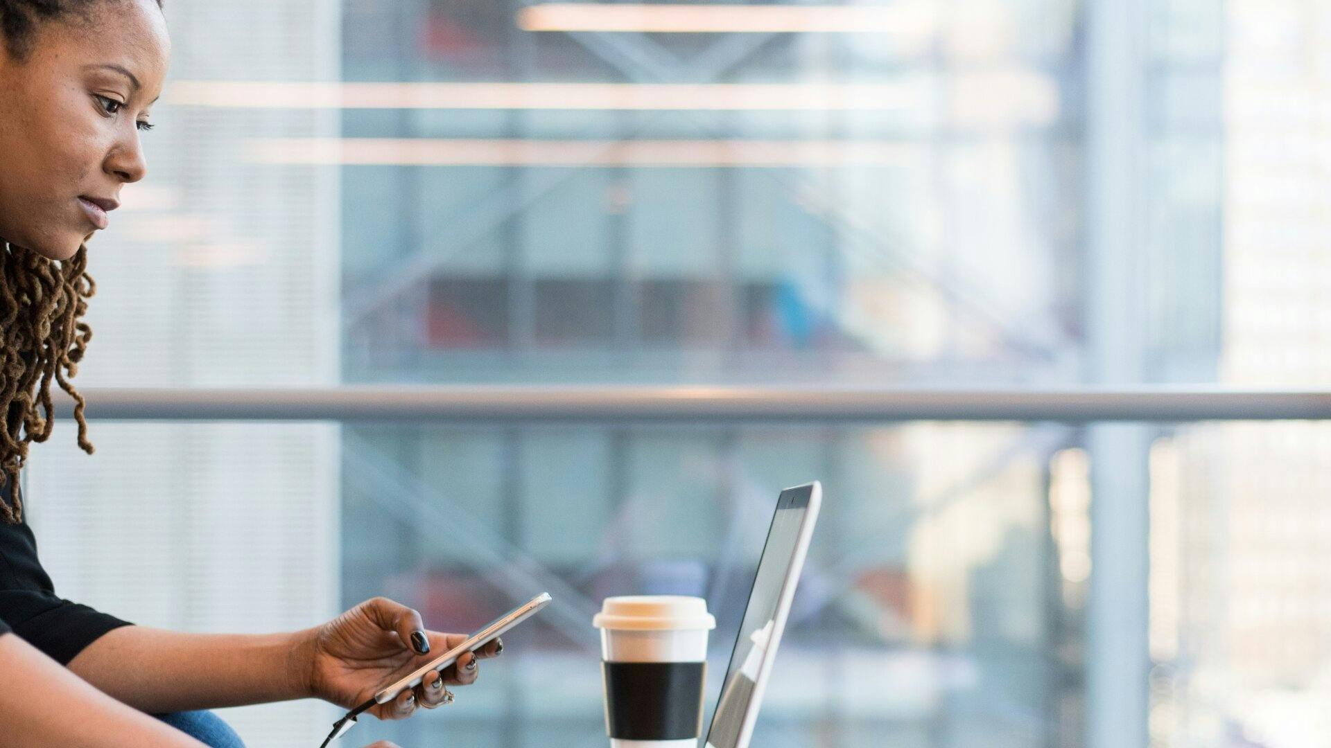 Jeune femme qui regarde son ordinateur en même temps qu’elle compose un appel sur son téléphone