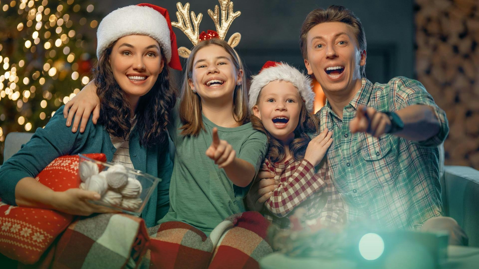 Des parents avec leurs deux fillettes, riant en regardant un film de Noël depuis leur sofa