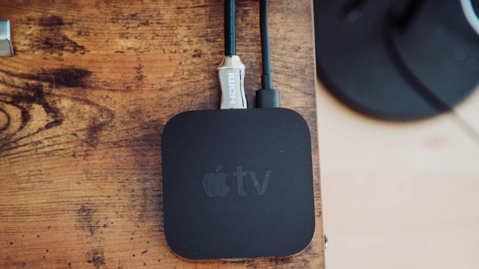 Vue aérienne d’une table en bois où on voit le boitier noir d’une Apple TV connectée à des fils