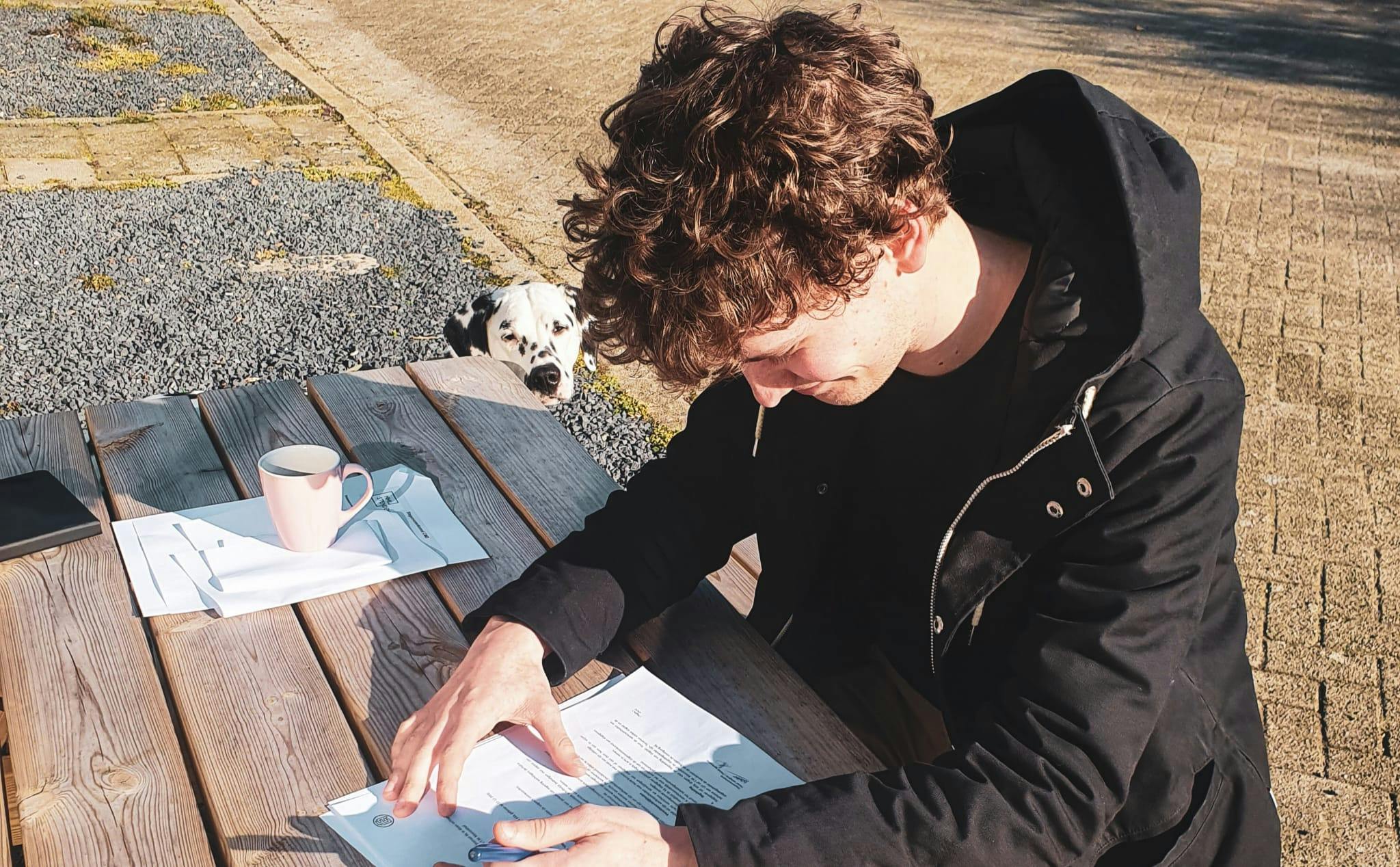 Jongen buiten aan tafel die een vragenlijst invult, met Oreo op de achtergrond