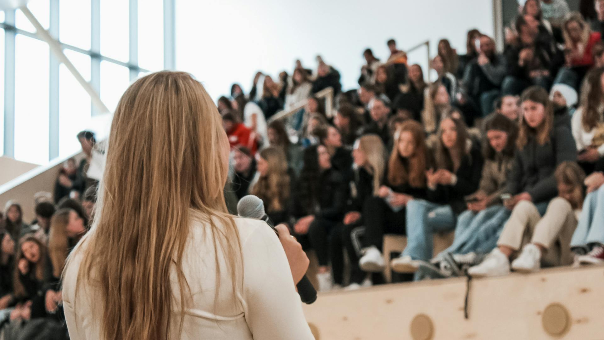 Mevrouw met microfoon voor een grote groep leerlingen