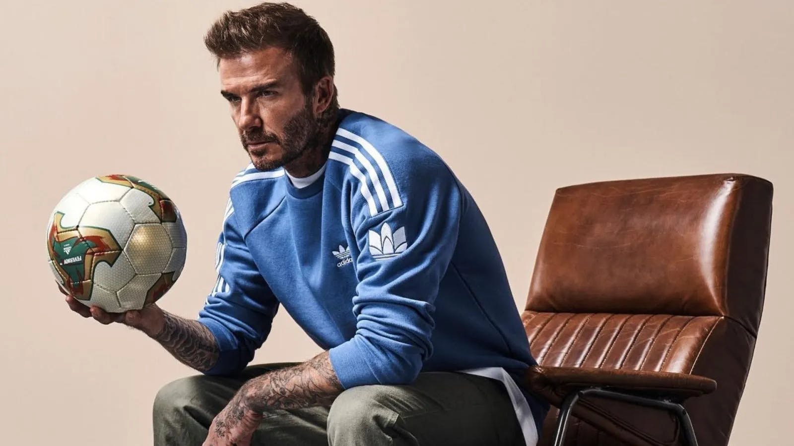 David Beckham sitting in a leather chair holding a football.