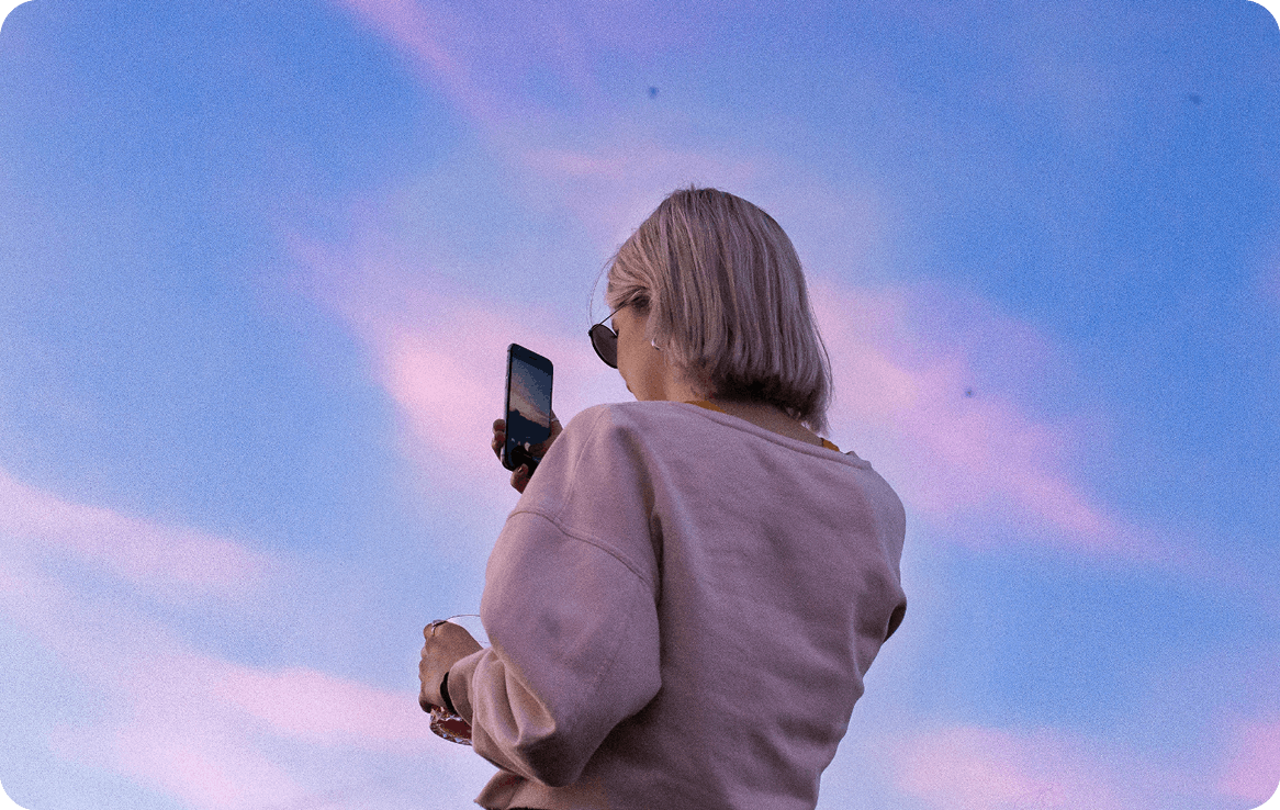 Blonde girl taking a photo with her mobile phone of a lilac sunset.