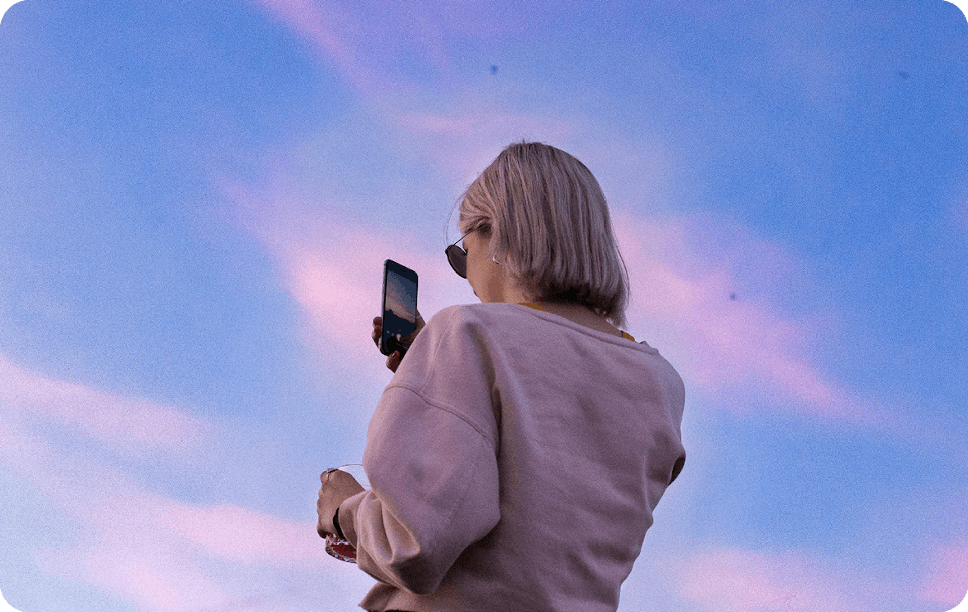 Blonde girl taking a photo with her mobile phone of a lilac sunset. 